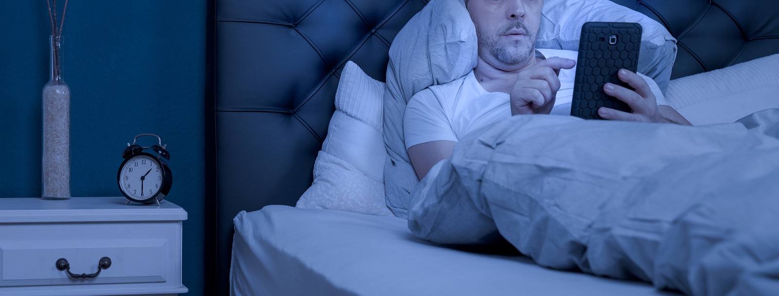 Man lying in bed on his phone representing the struggle with insomnia. Insomnia can lead to a breakdown in both physical and mental health. If you are struggling insomnia treatment in Arizona can help restore your sleep routine.