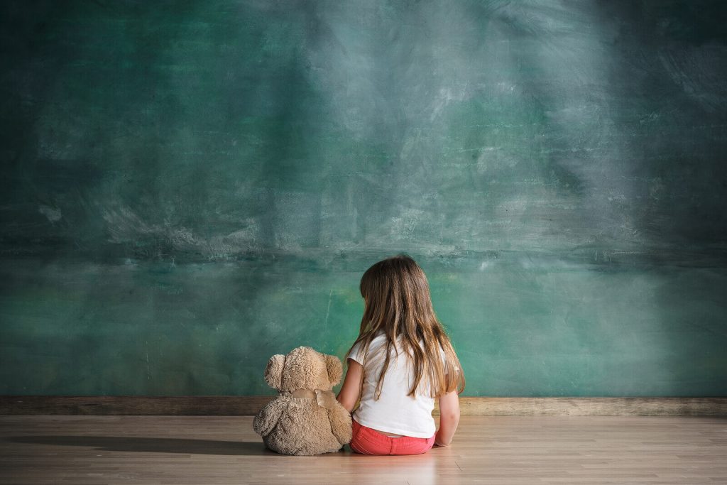 Little girl struggling with ADHD sitting alone with her teddy bear. ADHD can cause behavior issues that isolate children and leave them disconnected. Learn to manage these issues with ADHD treatment in Arizona. 
