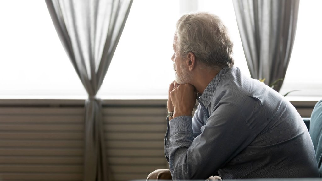 Sad older man looking pensively out the window representing someone dealing with depression who could benefit from Depression Treatment in Arizona.
