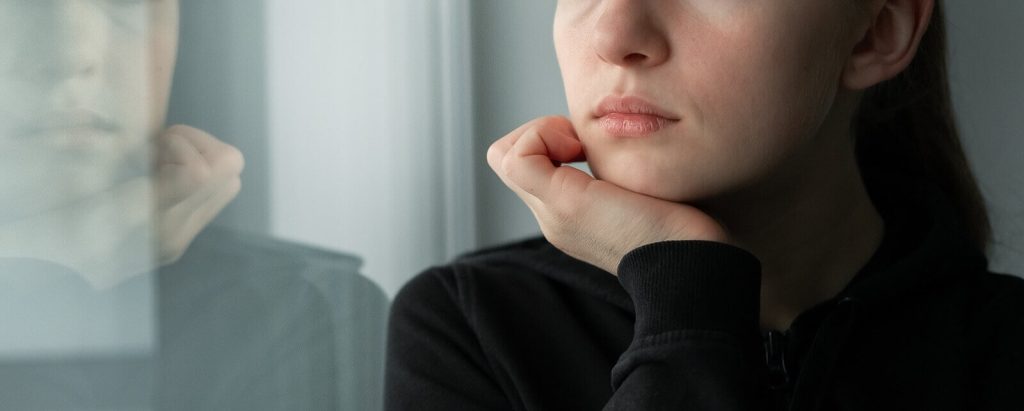 Young woman looking out the window while battling treatment resistant depression. Depression Treatment in Arizona can help you win this battle. 